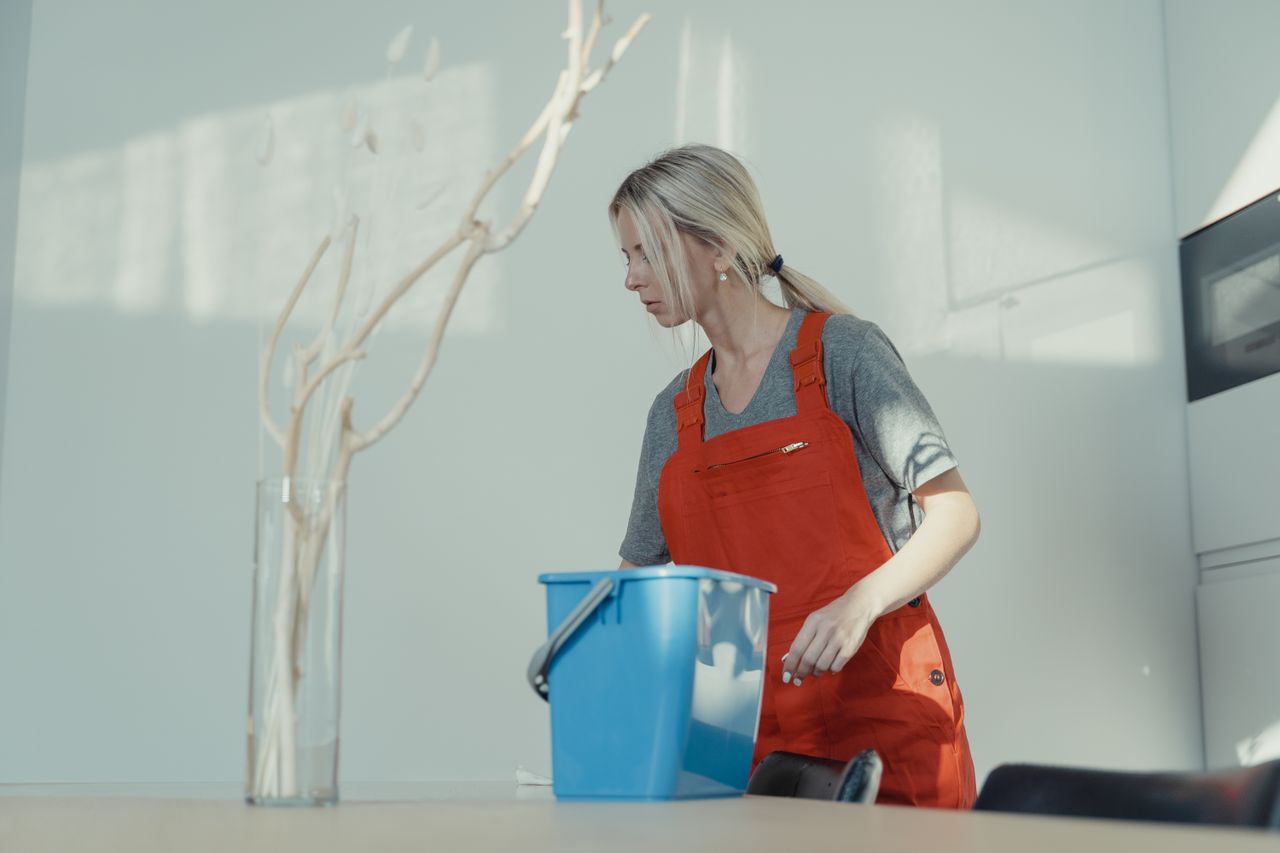 Une femme en uniforme rouge nettoie à l’intérieur avec un seau bleu, afin d’assurer un environnement impeccable.